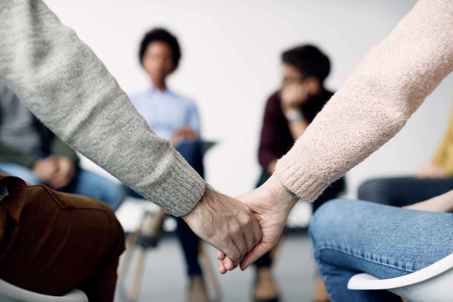 Close-up of two people holding hands during group therapy