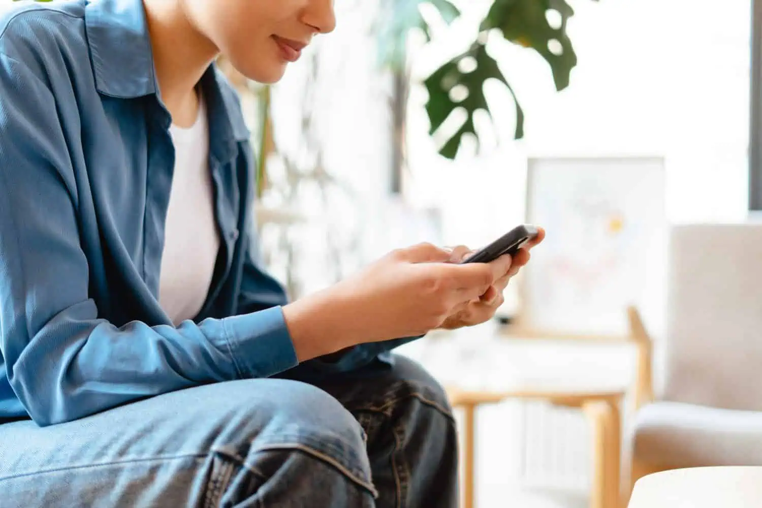 Smiling young woman holding mobile phone, using smartphone at home