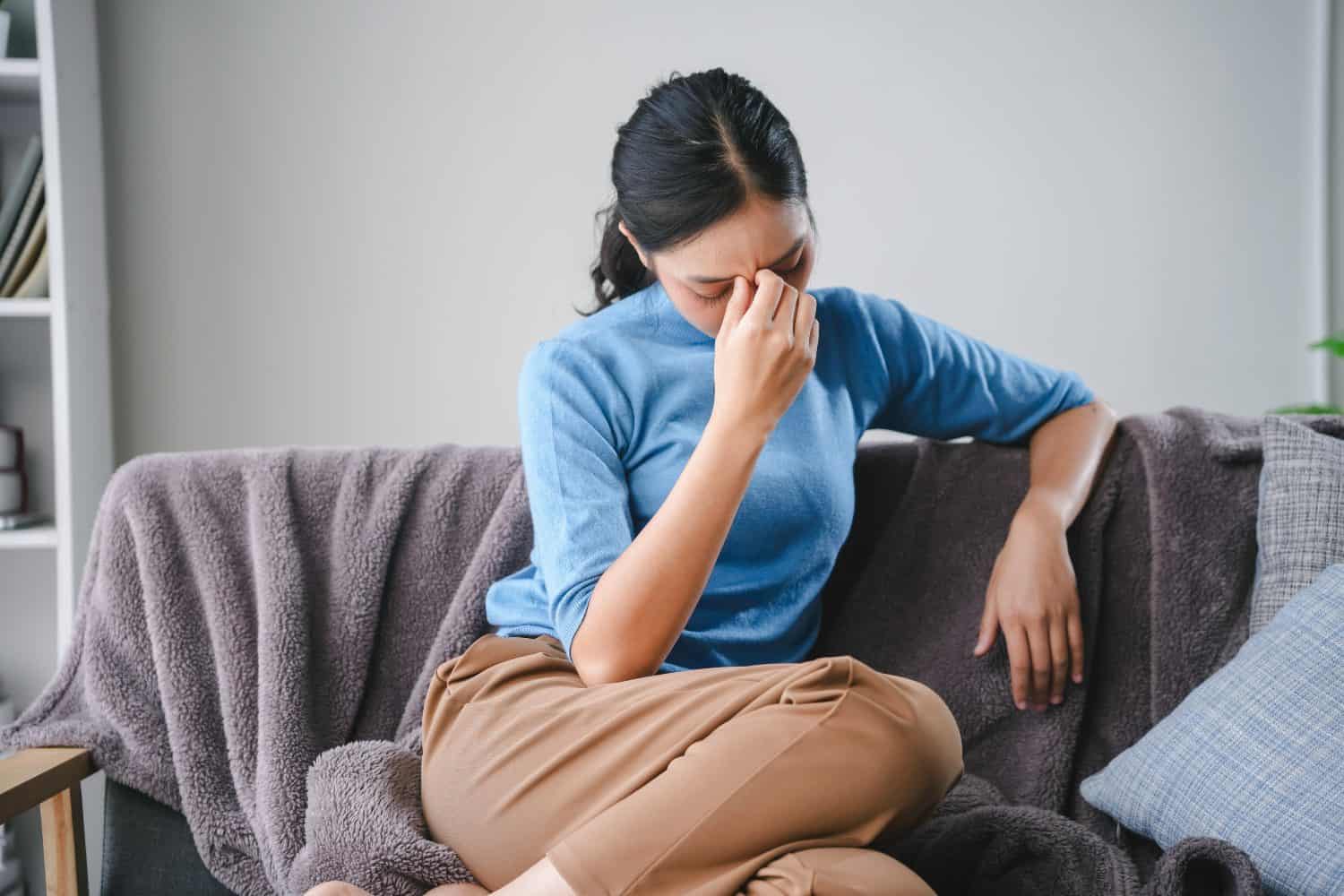 Stressed young woman massages temples at home, feeling tired and anxious.