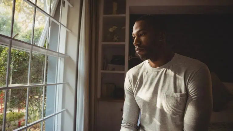 Thoughtful man sitting by window at home, concept of willpower and mental health