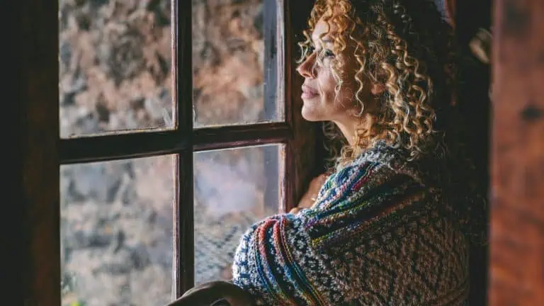 Woman Gazing Thoughtfully Out Window In Quiet Home