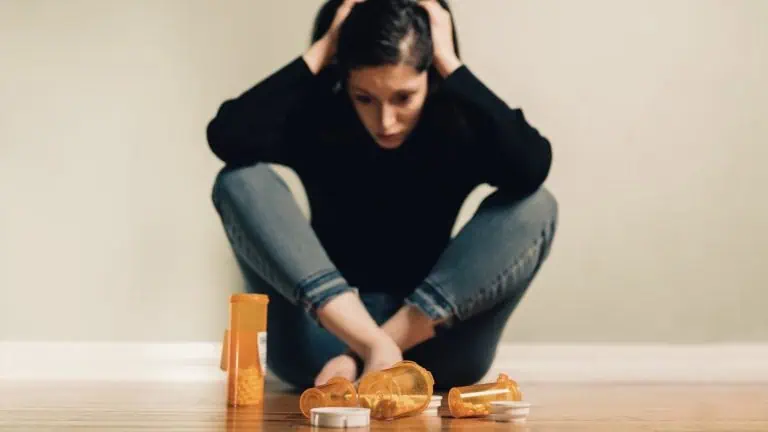 Young woman looking depressed sitting next to a bunch of pill bottles