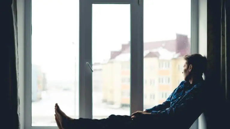 a sad man with depression sitting by the window, looking outside