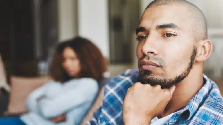 focused shot of a man looking contemplative while a blurred image of a woman is in the background