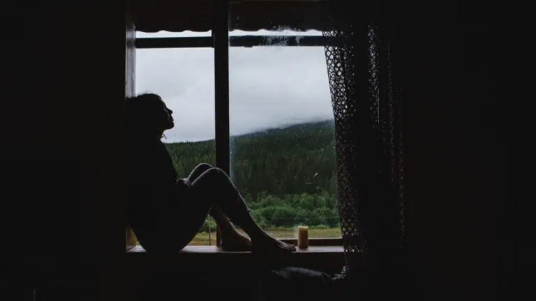 girl is sitting on the windowsill, concept of isolation, depression, mental health concern