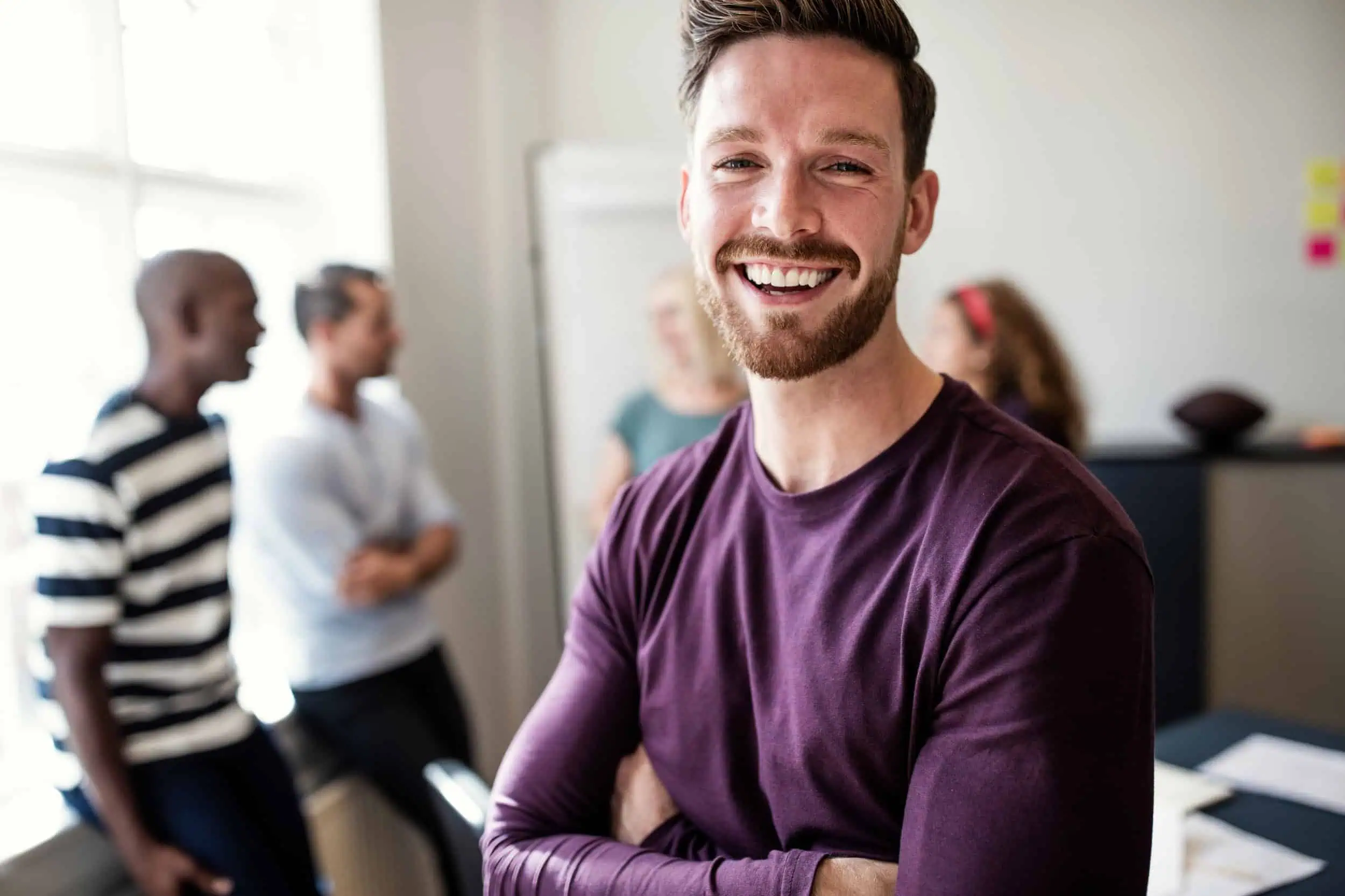 laughing man in focus with work meeting in the background, concept of wellness and recovery
