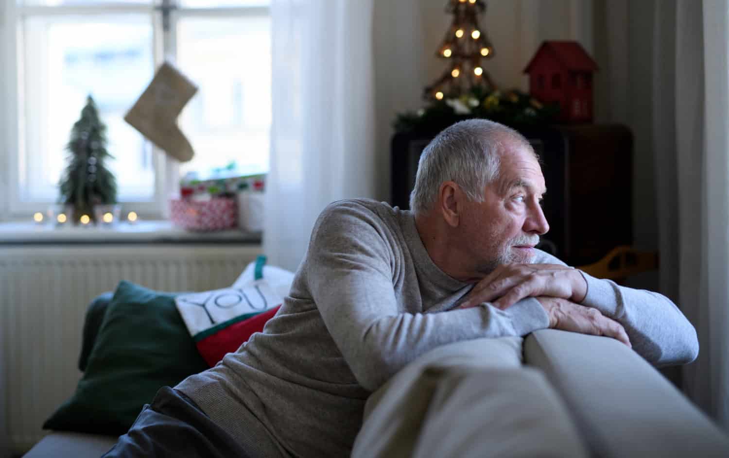 senior man sitting on sofa indoors at Christmas, solitude concept