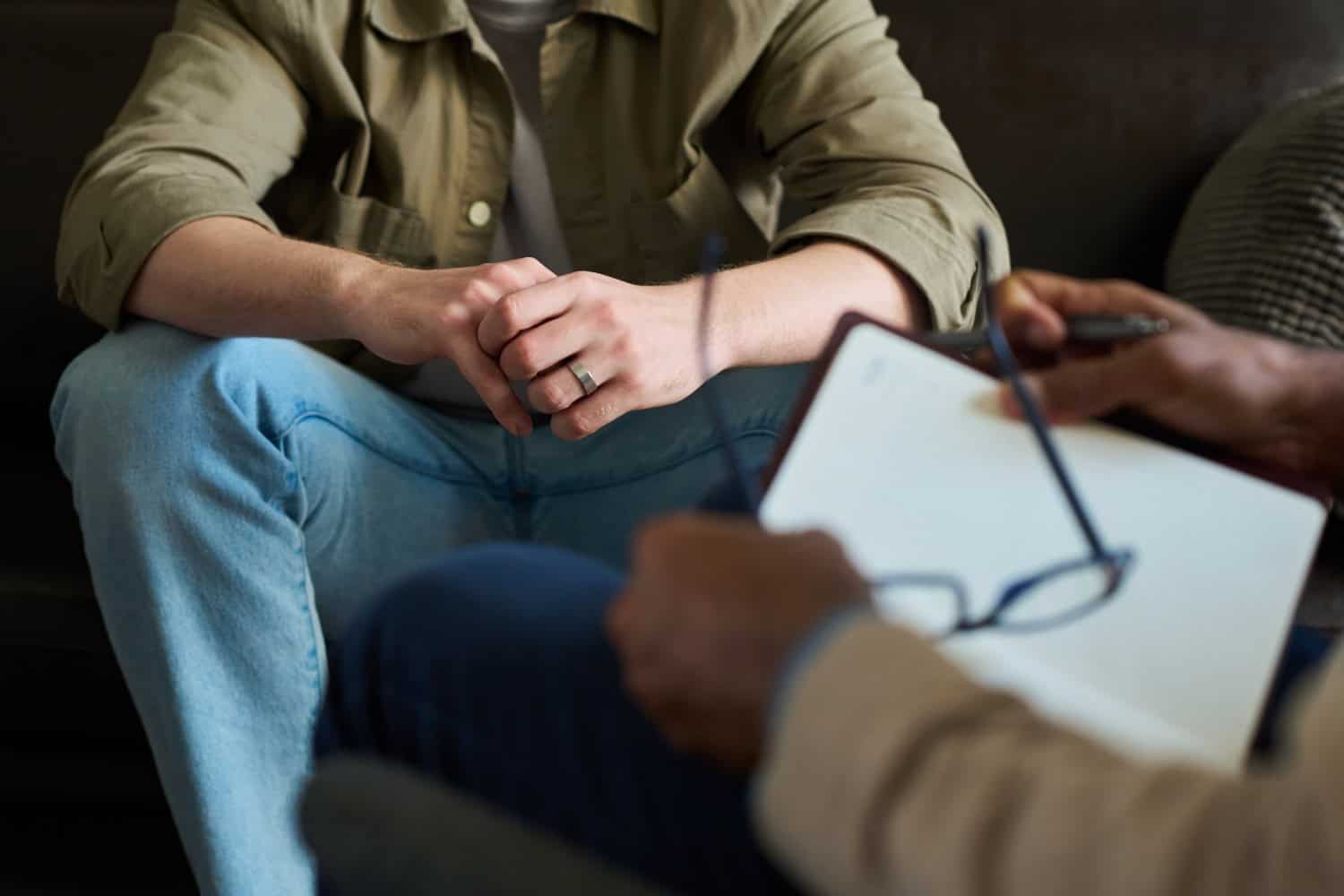 two adults sit indoors with one taking notes as the other talks, concept of counseling