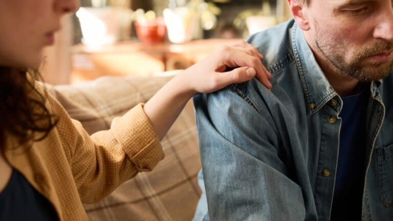 wife comforting husband in a gesture of touching his shoulder, concept of family support