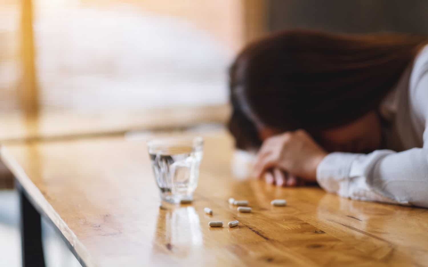woman sleep on table with white pills and a glass of water, addiction concept, self-medication