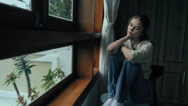 woman struggling with depression sitting by the window and looking outside