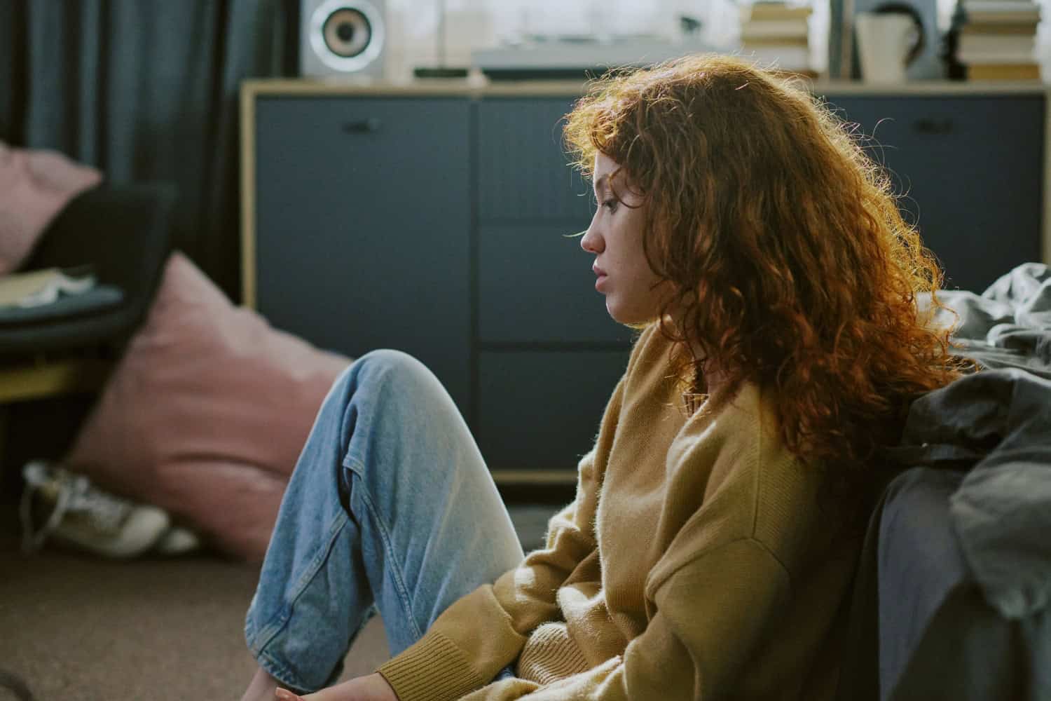 young woman looking sad and depressed while sitting alone in a messy room